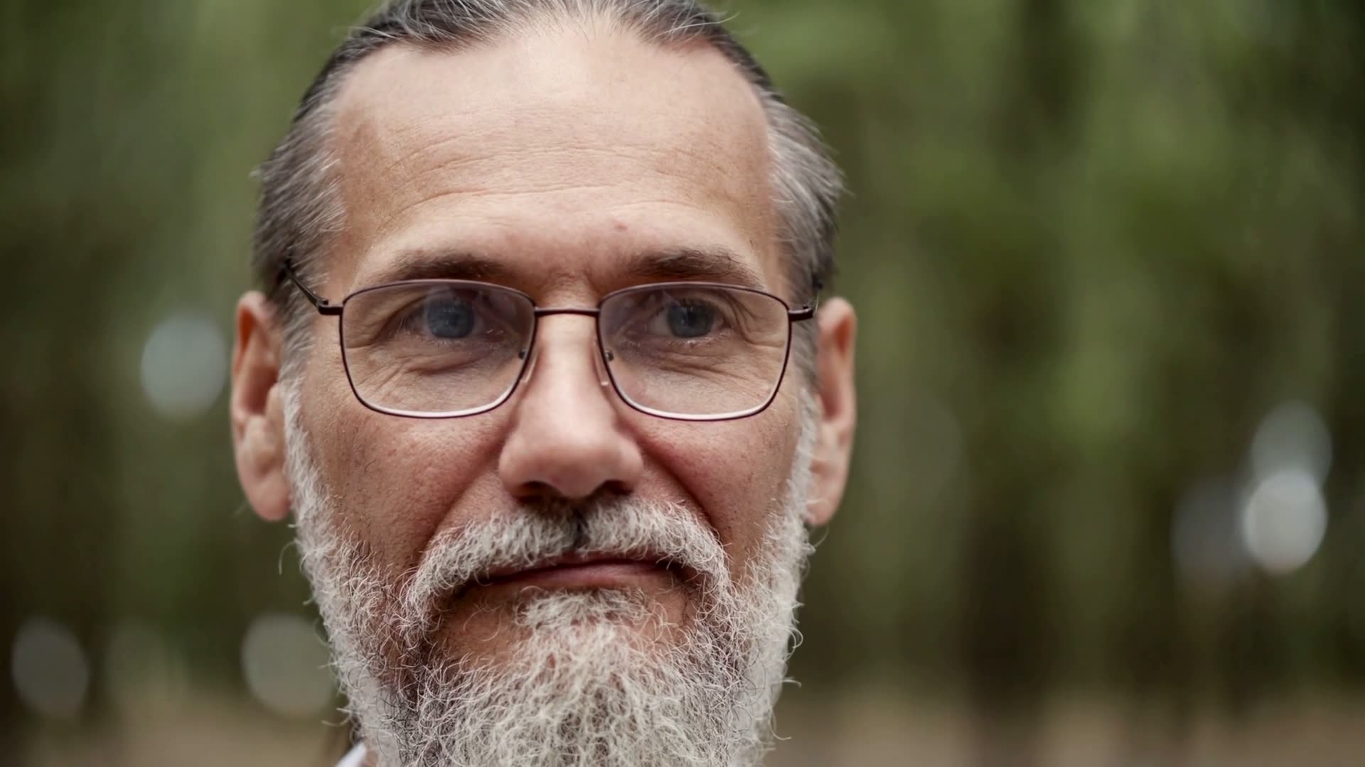 Um homem de barba grisalha e óculos, a pensar
